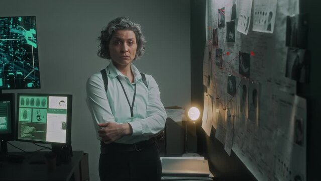 Medium portrait of Caucasian female police detective or special agent, posing with folded arms in bureau office, next to crime map, looking at camera with stressed heavy frown