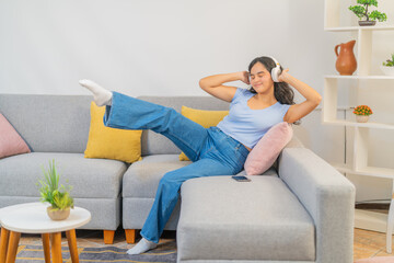 Obraz premium Happy latin woman listening to music sitting on the sofa