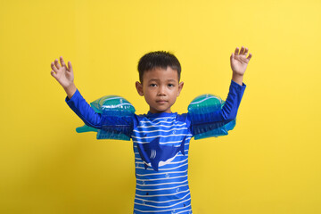 Portrait of a cute little Asian boy wearing a swimsuit posing with both hands raised isolated on a...