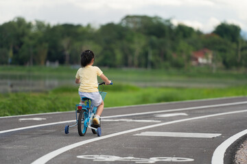Fototapeta premium Back side view of asian baby girl child learning to ride bicycle in the park garden. Education concept for kid practiice cycling at park, baby sport concept.