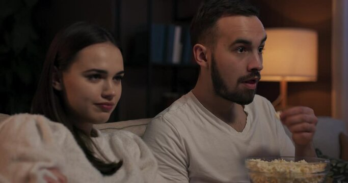 Lovely couple watching romantic comedy filled with cheesy lines awkward moments woman annoyed by man's loud chewing can't focus on movie while the man oblivious to annoyance continue eat popcorn.