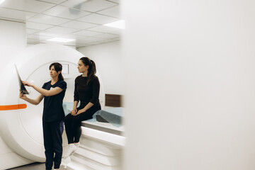 Doctor and patient are discussing results of tomography eximination. Female doctor is scrolling scrren of tablet and analizing scans of brain. Woman is sitting and listens attentively to doctor.