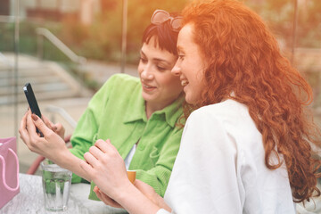 Two women laughing together while looking at a phone screen in a cafe