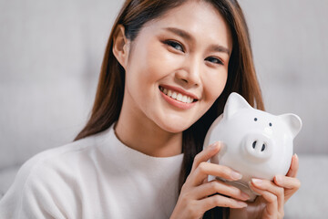 Young Asian woman with white piggy bank, Indoors.