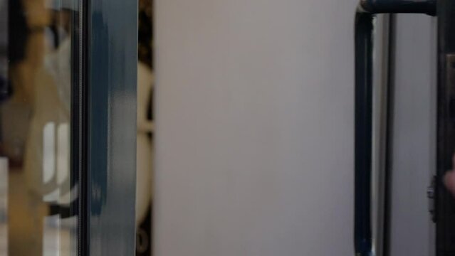 Close-up of a hand in a purple sleeve pulling a door handle, focusing on the grip and motion of opening the door. The background is blurred, highlighting the hand's action.