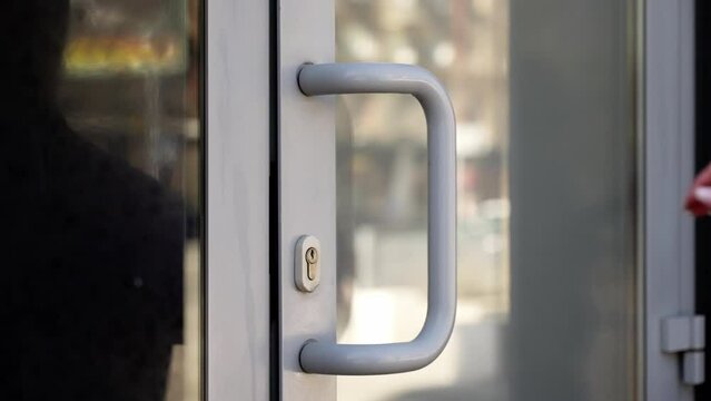Close-up of a hand in a purple sleeve pushing a light-colored door handle, focusing on the grip and motion, with a blurred background for emphasis.