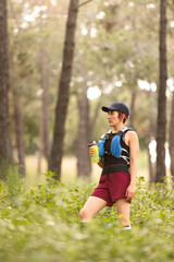 A woman wearing a red jacket and blue vest holding a bottle and a water bottle. She is wearing a black hat