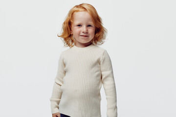 Fashionable little girl with red hair in white turtleneck sweater and black pants standing...