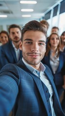 Obraz premium A young businessman in a suit taking a selfie with a group of his workers in his office space