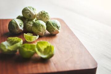 Brussels sprouts, wooden board and cooking in kitchen for health, lunch and nutrition for wellness. Vegetables, food and chopping block on table, leaves and meal prep for dinner on vegan diet in home