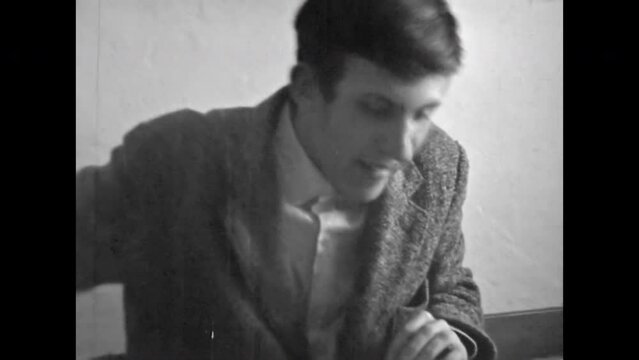 Archive film, student cheating on exam in university classroom. Funny young man studying in college. Student sitting at class desk, writing notes in notebook. Vintage black white retro education 1980s