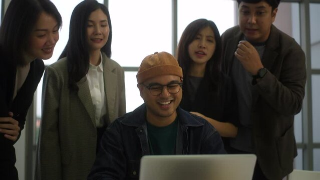 Happy asian business team brainstorming with teamwork using laptop computer at office, cheering young entrepreneur meeting with colleagues and planning discussion on project of software design.