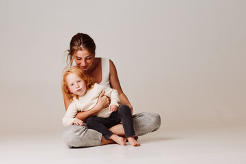 Family time a woman and a little girl sitting on the floor in front of a white background