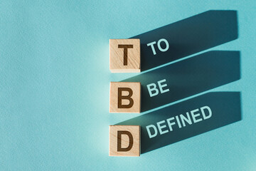 Wooden cubes with TBD meaning To Be Defined cast long shadows on a blue surface.