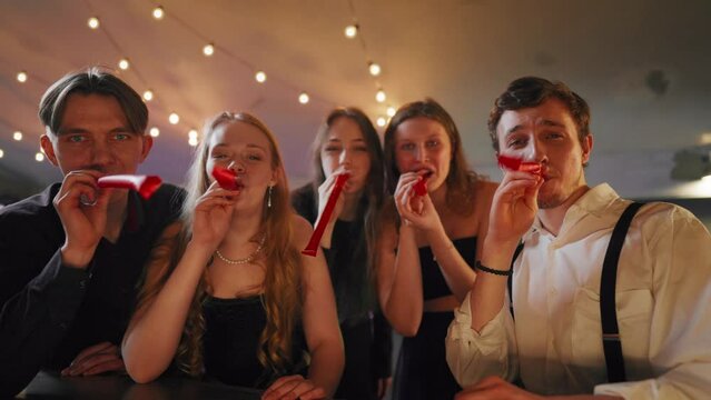 People celebrating b-day, blowing noisemakers whistles, congratulation party. Portrait of happy five best friends cheering and greeting, merry birthday party, gathering in festival in nightclub