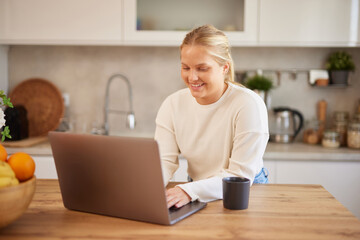 Young woman wearing casual clothes using laptop and drinking coffee in the kitchen