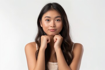 Fototapeta premium Portrait of a young woman with long dark hair, looking at the camera with hands near her face against a plain white background.