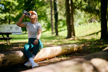 Thirsty sportswoman drinking water from  bottle while exercising in nature.