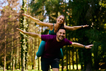 Playful athletic couple piggybacking with arms outstretched in nature.
