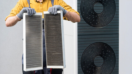 Worker in gloves holding two dirty air filters from a home ventilation system.