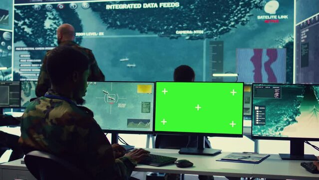Private monitors national guard activity with military CCTV satellite system, working with a greenscreen display on pc in command center. IT reconnaissance operator tracking ships. Camera B.
