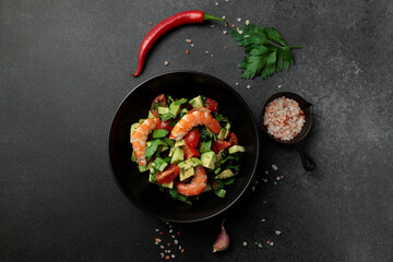 Salad of king prawns, avocado, cucumber, tomato and herbs. Black background