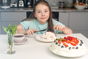 Cute little pre-teen girl eating a beautiful berry dessert or cake while sitting at home in front of the kitchen. Selected focus.