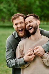 Two bearded men, a loving couple, share a laugh while embracing in a green park.