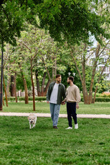 Fototapeta premium A bearded gay couple walks hand-in-hand through a verdant park with their labrador retriever.