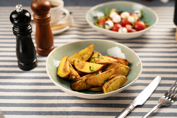 Fried potatoes and fresh vegetable salad for dinner served on a table with a striped tablecloth and...