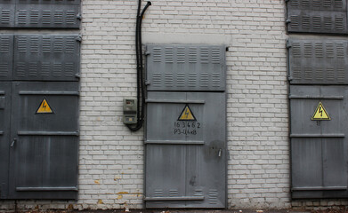Three Grey Metal Doors With High Voltage Signs On A White Brick Wall Texture Background

