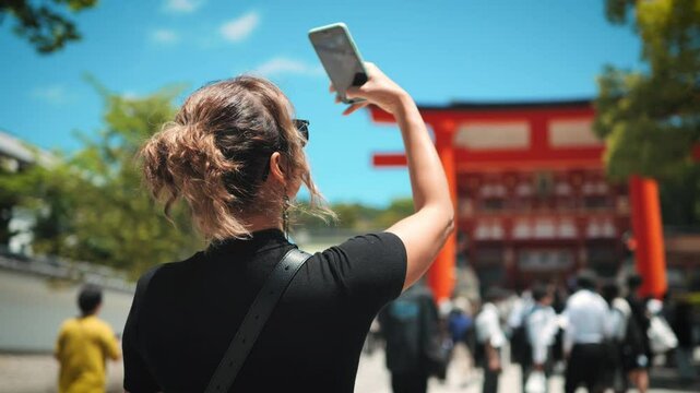Woman in a black outfit stands in a corridor of red torii gates, creating a striking perspective with vibrant colors. She explores the famous Fushimi Inari Shrine, immersed in the cultural experience