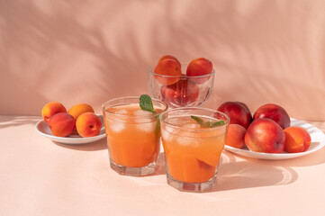 Healthy vitamin summer fruit nutrition, peaches, nectarines and apricots on plate, glasses with iced cocktail or juice drinks on bright pink background with sunlight shadows