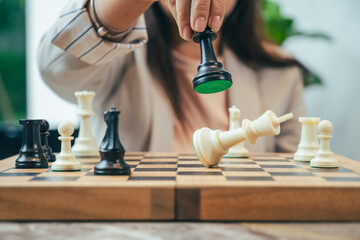 The close-up of a businesswoman’s hand making a checkmate move on a chessboard. The background shows an office setting, emphasizing the parallel between chess strategy and business acumen.