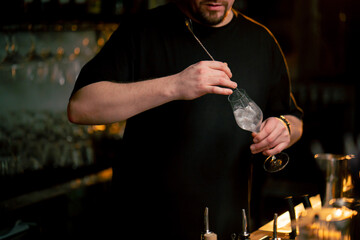 A professional bartender stirs white cocktail with ice in a beautiful glass in his hand