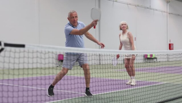 Two pickleball players prepare to return a ball on a pickleball court indoor