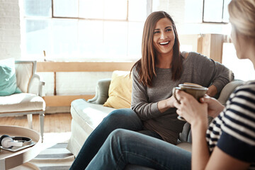 Happy woman, friends and talking with coffee on sofa for catch up, social or bonding in living room at home. Young female person with smile for morning, drink or conversation in friendship at house