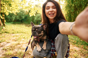 Hand holding camera, doing selfie. Young pretty woman is with her dog in the park