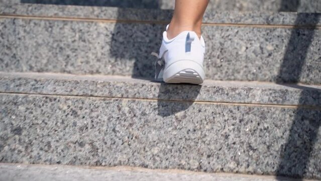 Close-up female teenager girl legs with sport shoes sneakers climd step the stairs. Rear view. Woman hurry up walking staircase sunny warm weather outdoors