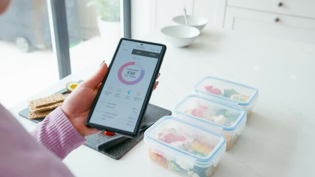 Close up of woman preparing healthy meals in kitchen at home looking at calorie counting app on mobile phone - shot in slow motion