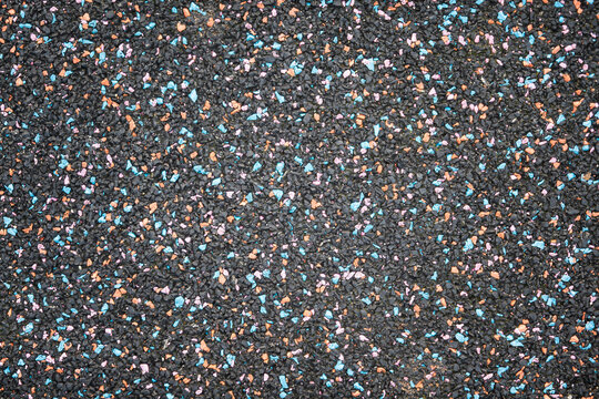 Sports surface made of black rubber crumb. There are bright colored blue and orange particles. Close-up. Background. Texture.