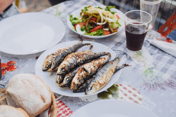 A bunch of grilled sardines on a plate, traditional salad, sangria, bread on a table. Saint Anthony...