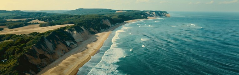 Aerial view of a long sandy beach stretching alongside the ocean waves near a towering cliff
