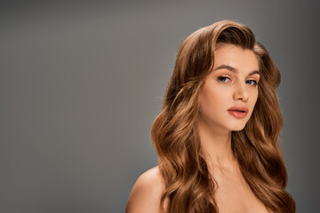 Naklejka premium A young beautiful woman with long, wavy hair elegantly posing on gray backdrop