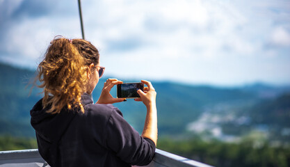 Young tourist woman using smart phone in the mountains, taking pictures. Girl makes a photo on the hiking on a summer sunny day. Girl using cell phone photography app.