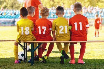Football Soccer Players in the Youth Team. Sports Teammates Sitting Together on a Wooden Bench. School Boys in Red and Yellow Soccer Jersey Shirts. Football Coach Coaching Junior Level Team