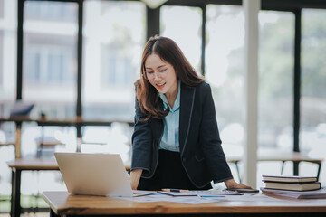 Young Asian professional business woman office worker analyst sitting at desk working on laptop thinking on project plan, analyzing marketing or financial data online, watching elearning webinar.