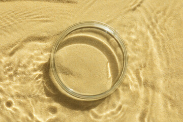 Stylish presentation for product. Glass podium in water on sand, top view