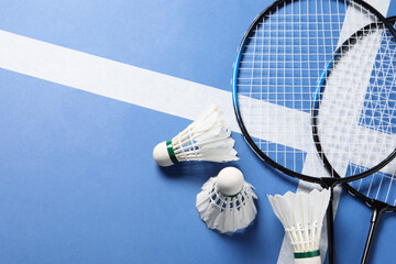 Feather badminton shuttlecocks and rackets on blue background, flat lay. Space for text