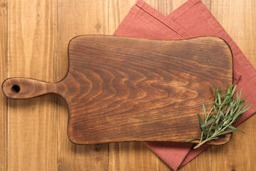 Cutting board, rosemary and napkin on wooden table, top view. Space for text